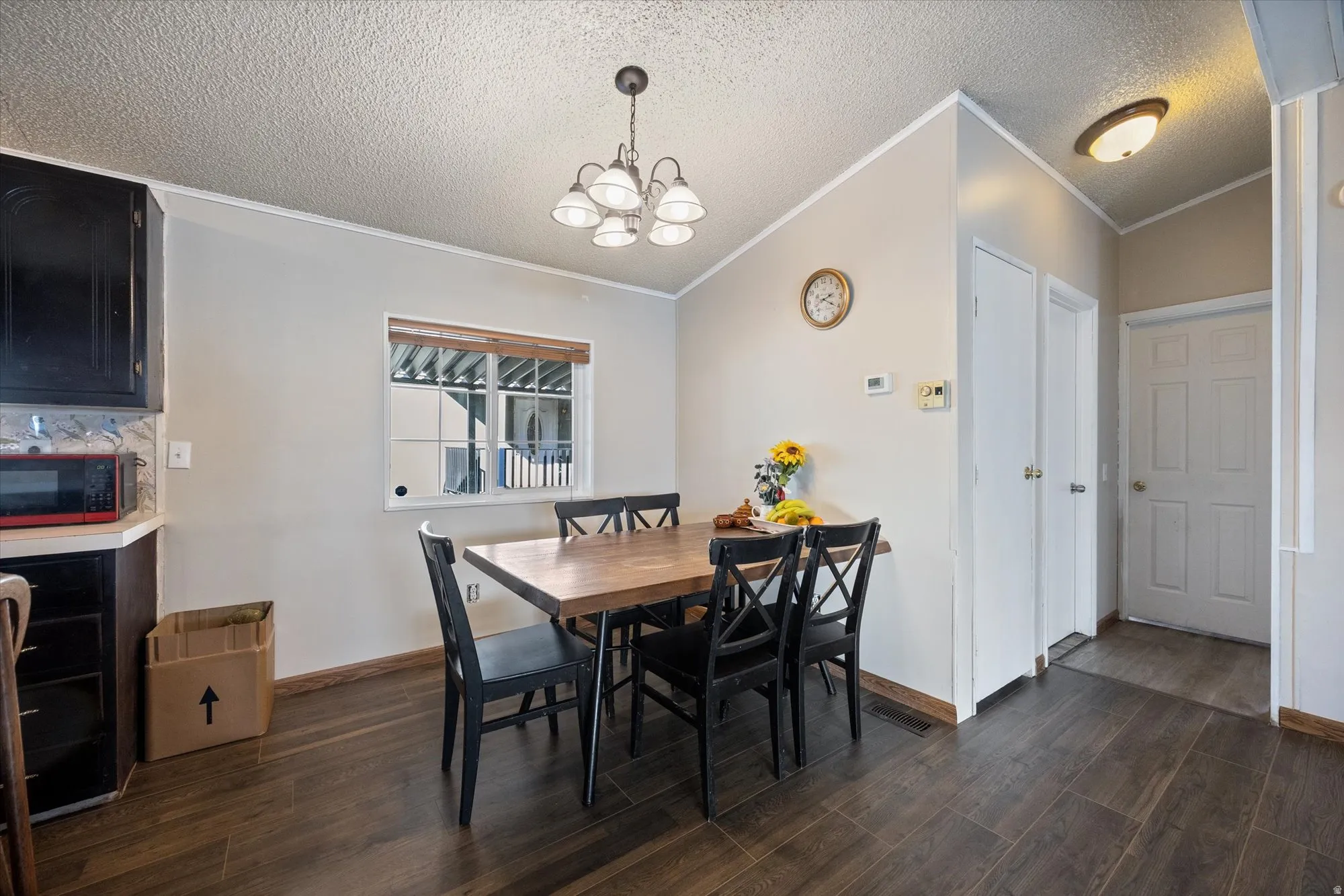 Dining room featuring dark wood finished floors, ornamental molding, a textured ceiling, a chandelier, and lofted ceiling