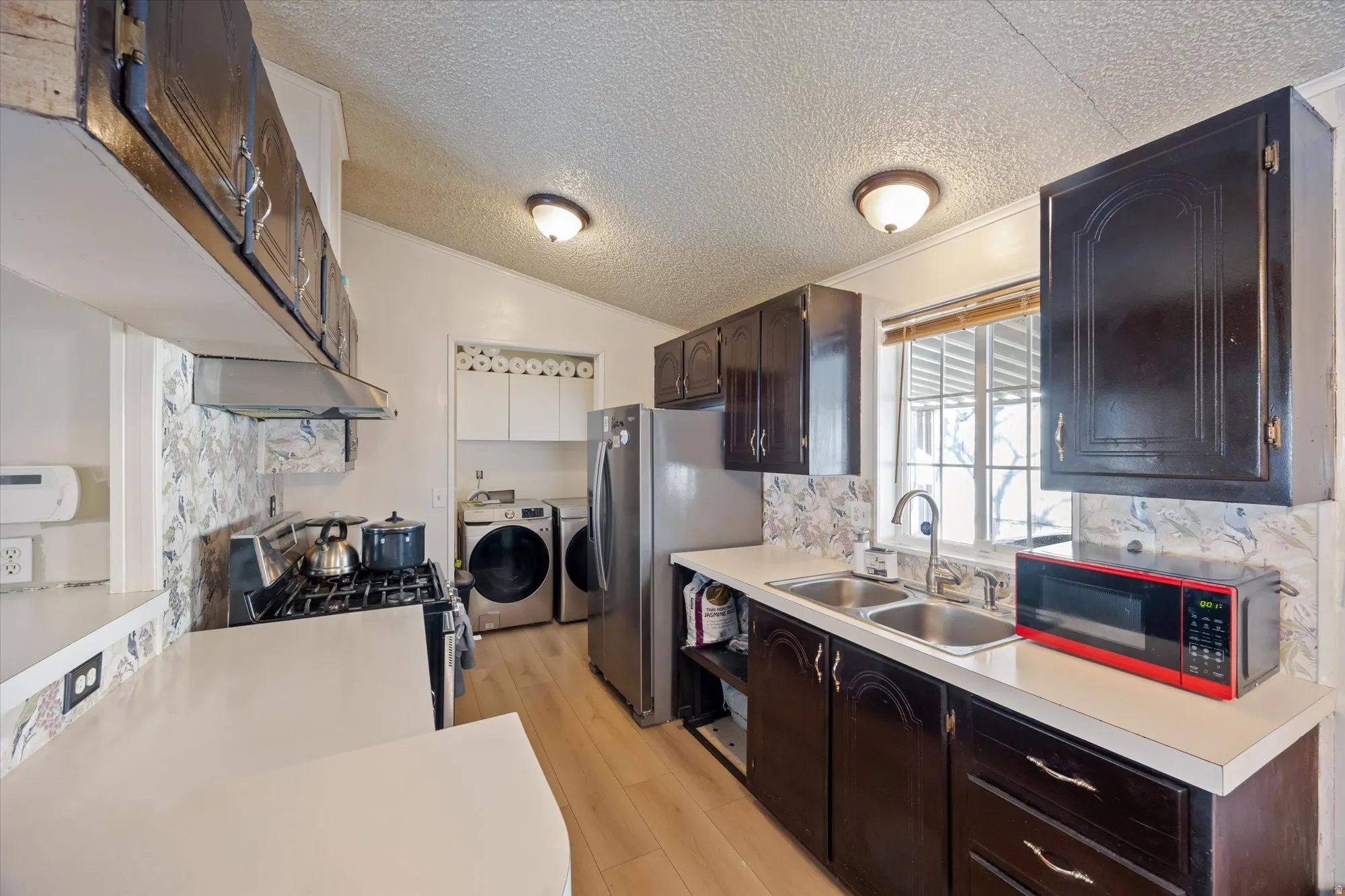 Kitchen with light countertops, stainless steel appliances, washer and clothes dryer, dark brown cabinets, and crown molding