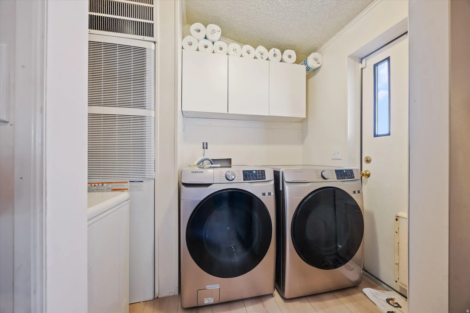 Washroom featuring a textured ceiling, a heating unit, washer and clothes dryer, cabinet space, and ornamental molding