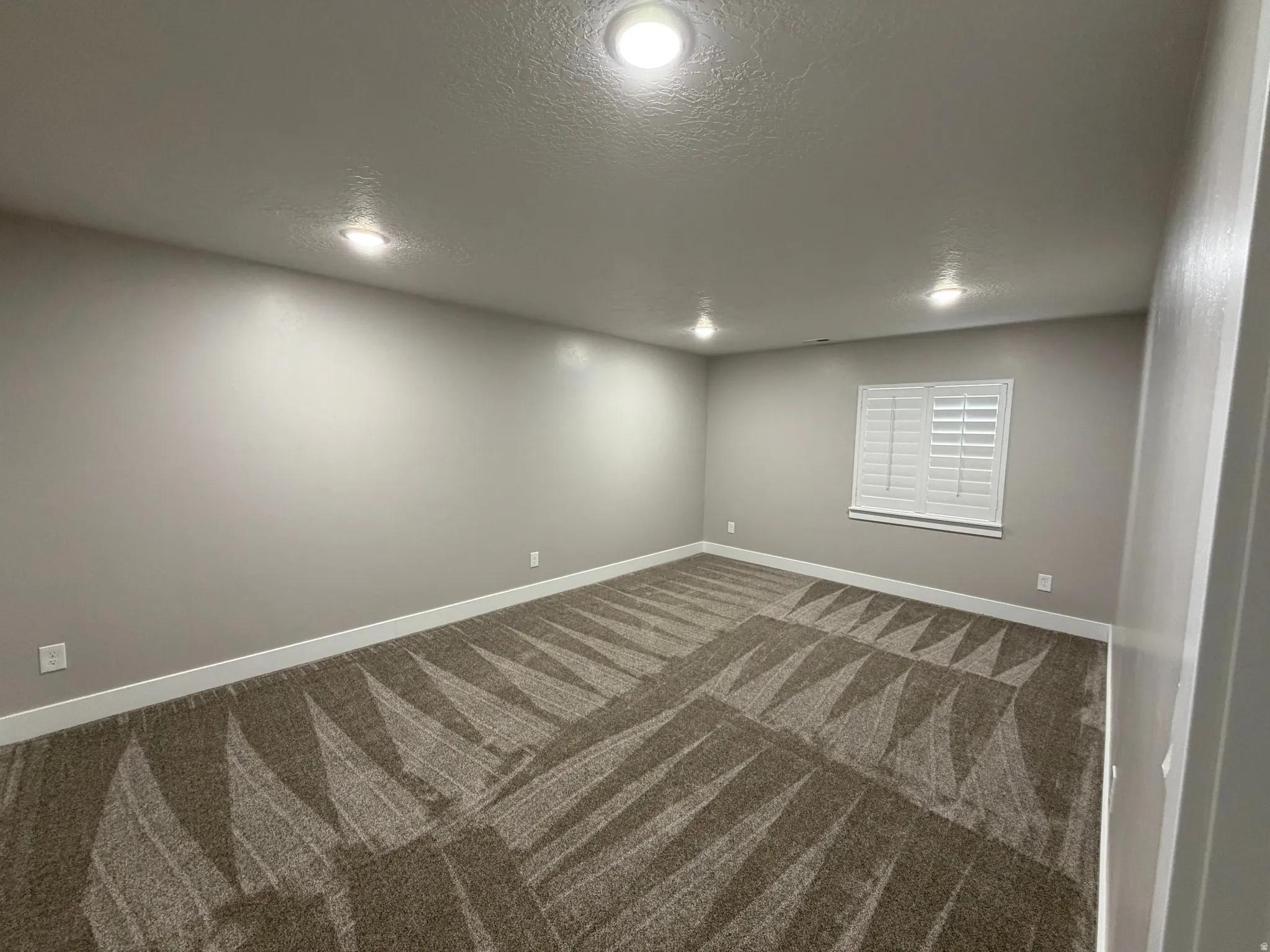 Empty room featuring a textured ceiling, carpet floors, and recessed lighting