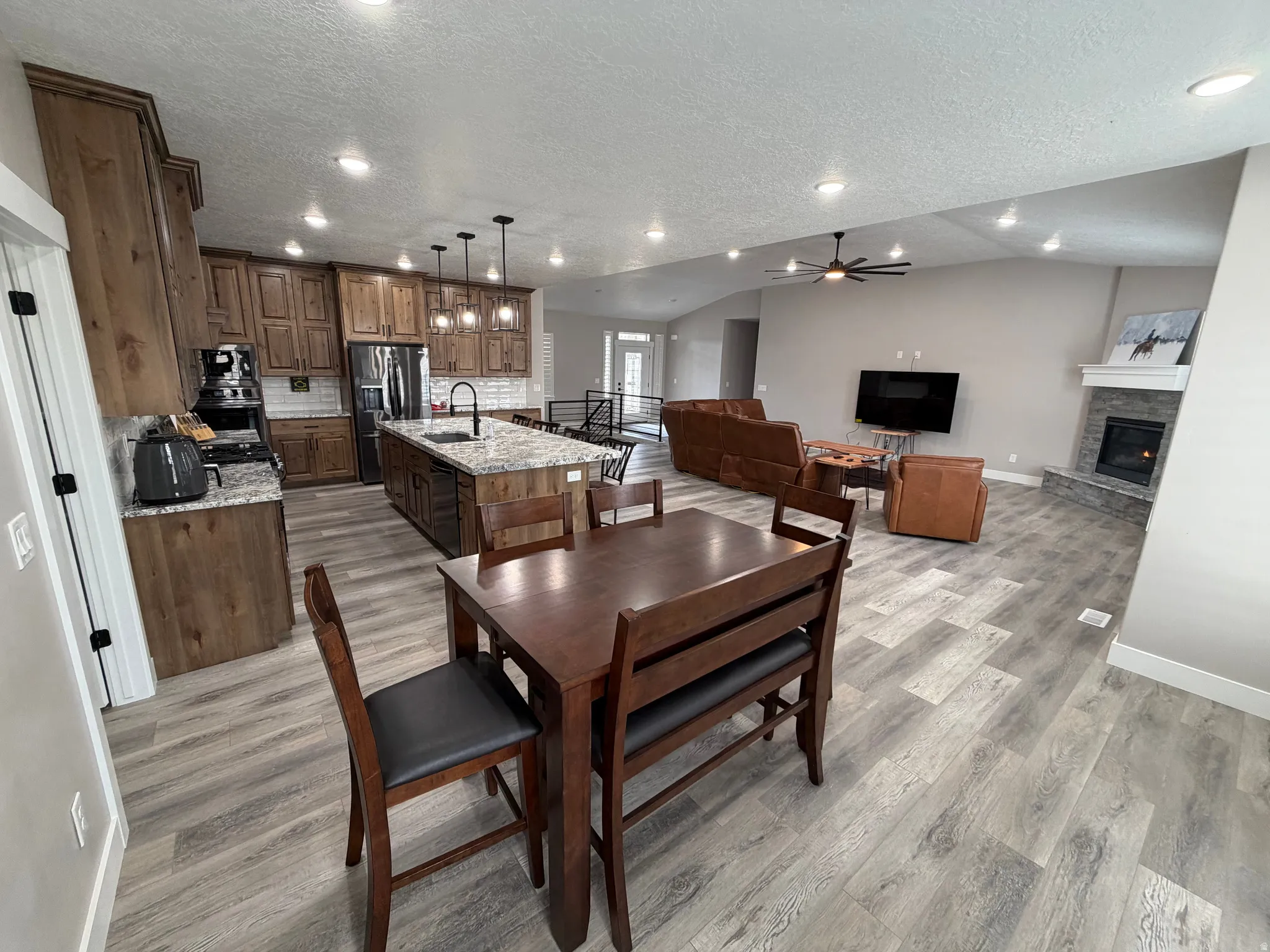 Dining room featuring a textured ceiling, ceiling fan, recessed lighting, light wood-style floors, and a stone fireplace