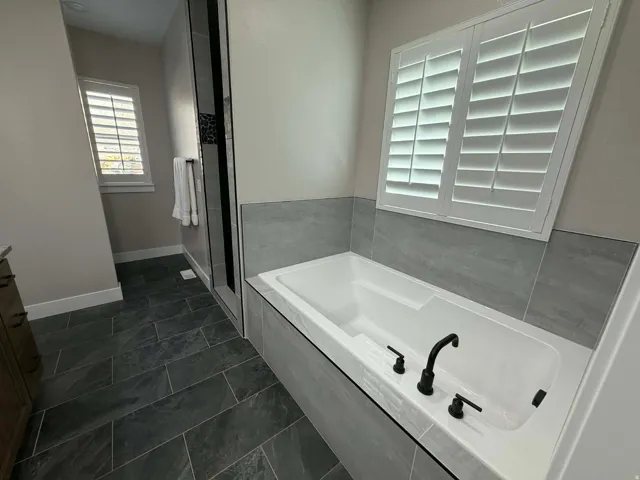 Bathroom with a garden tub, dark tile patterned floors, a stall shower, and vanity