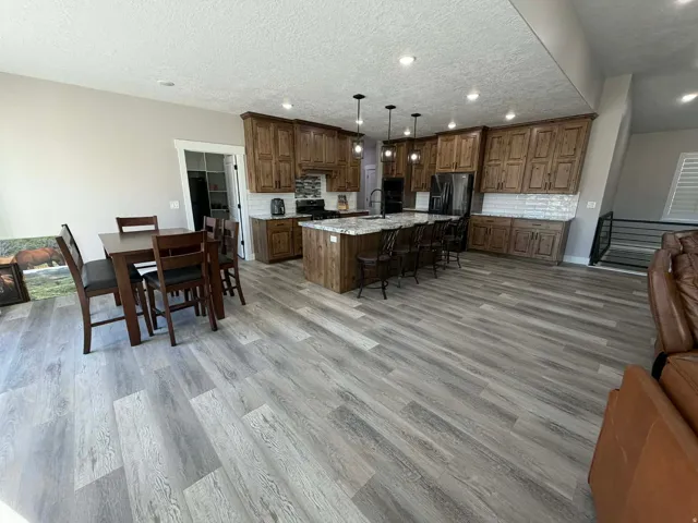 Kitchen with open floor plan, a breakfast bar area, an island with sink, tasteful backsplash, and a textured ceiling