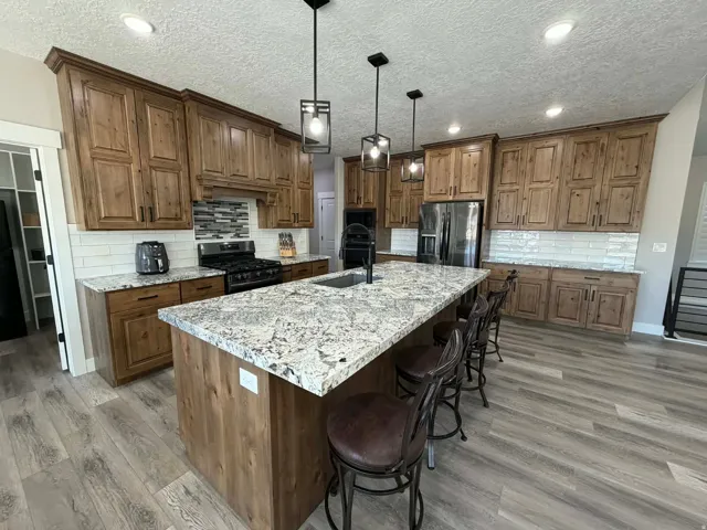 Kitchen featuring a textured ceiling, backsplash, brown cabinetry, a kitchen bar, and recessed lighting