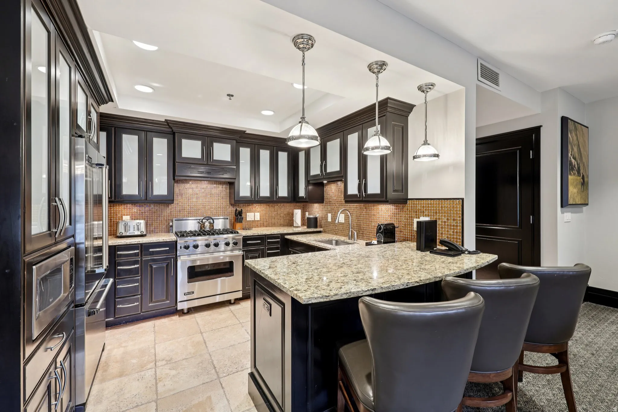 Kitchen with a breakfast bar, glass insert cabinets, a raised ceiling, light stone countertops, and premium appliances