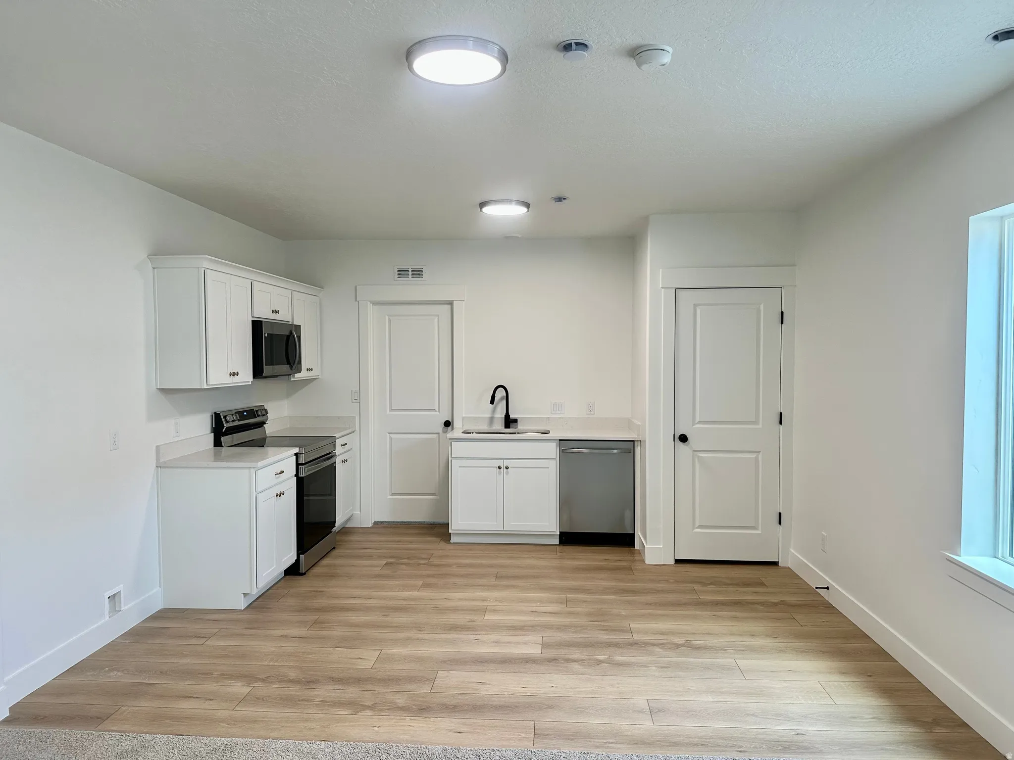Kitchen featuring white cabinets, stainless steel appliances, light countertops, and light wood finished floors