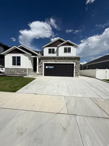Modern exterior design featuring stone and vertical siding, a two-car garage, concrete driveway, and a white fence