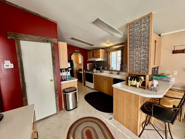 Kitchen with light countertops, white range with electric cooktop, a breakfast bar area, a textured ceiling, and under cabinet range hood