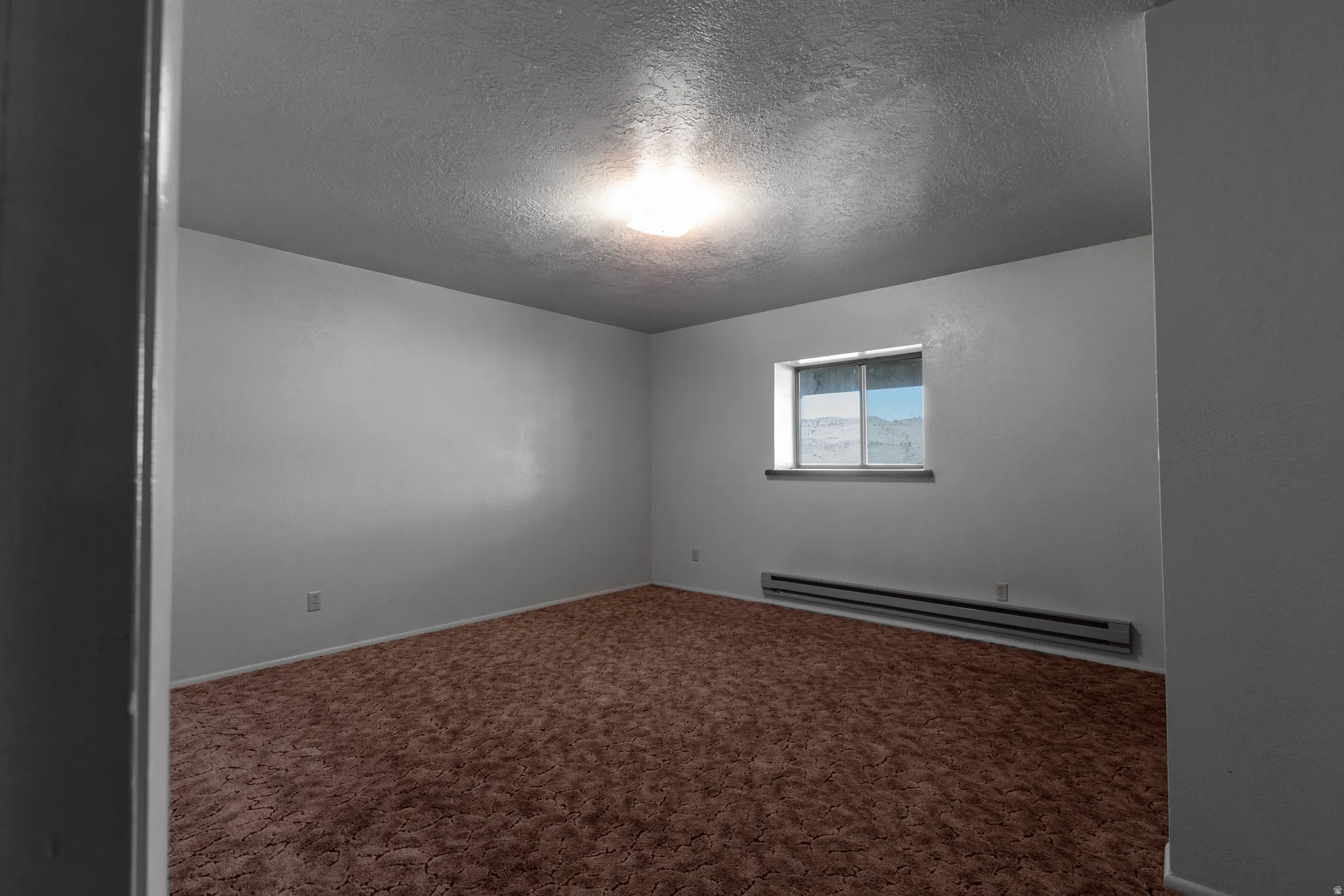 Empty room featuring a textured ceiling, baseboard heating, and carpet