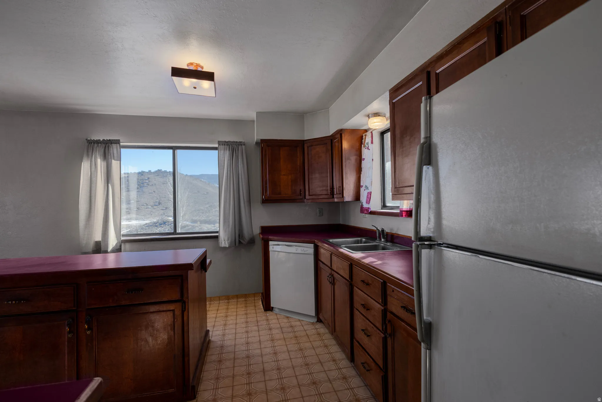 Kitchen featuring freestanding refrigerator, light flooring, white dishwasher, dark countertops, and dark brown cabinetry
