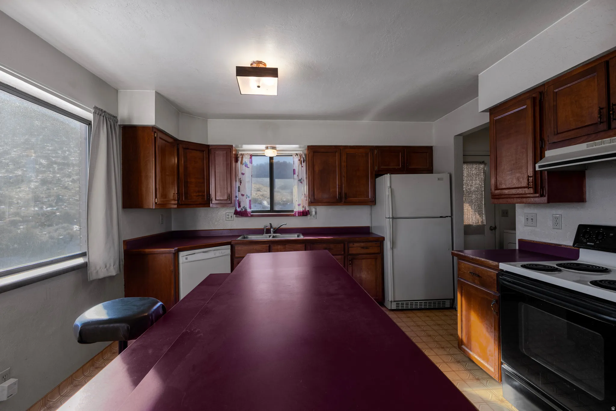 Kitchen with light flooring, white appliances, dark countertops, and under cabinet range hood