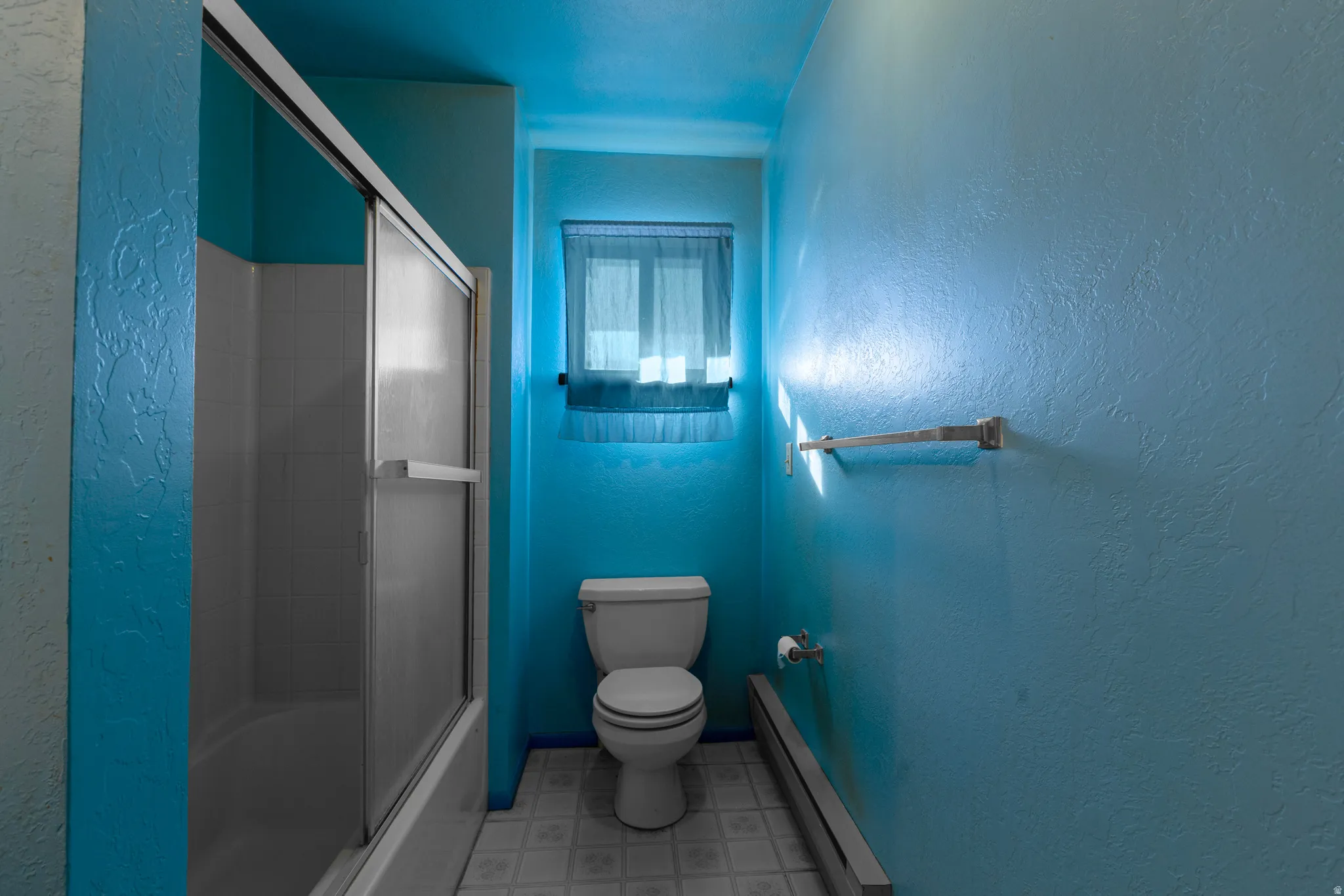 Bathroom with a textured wall, a baseboard heating unit, shower / bath combination with glass door, and light floors