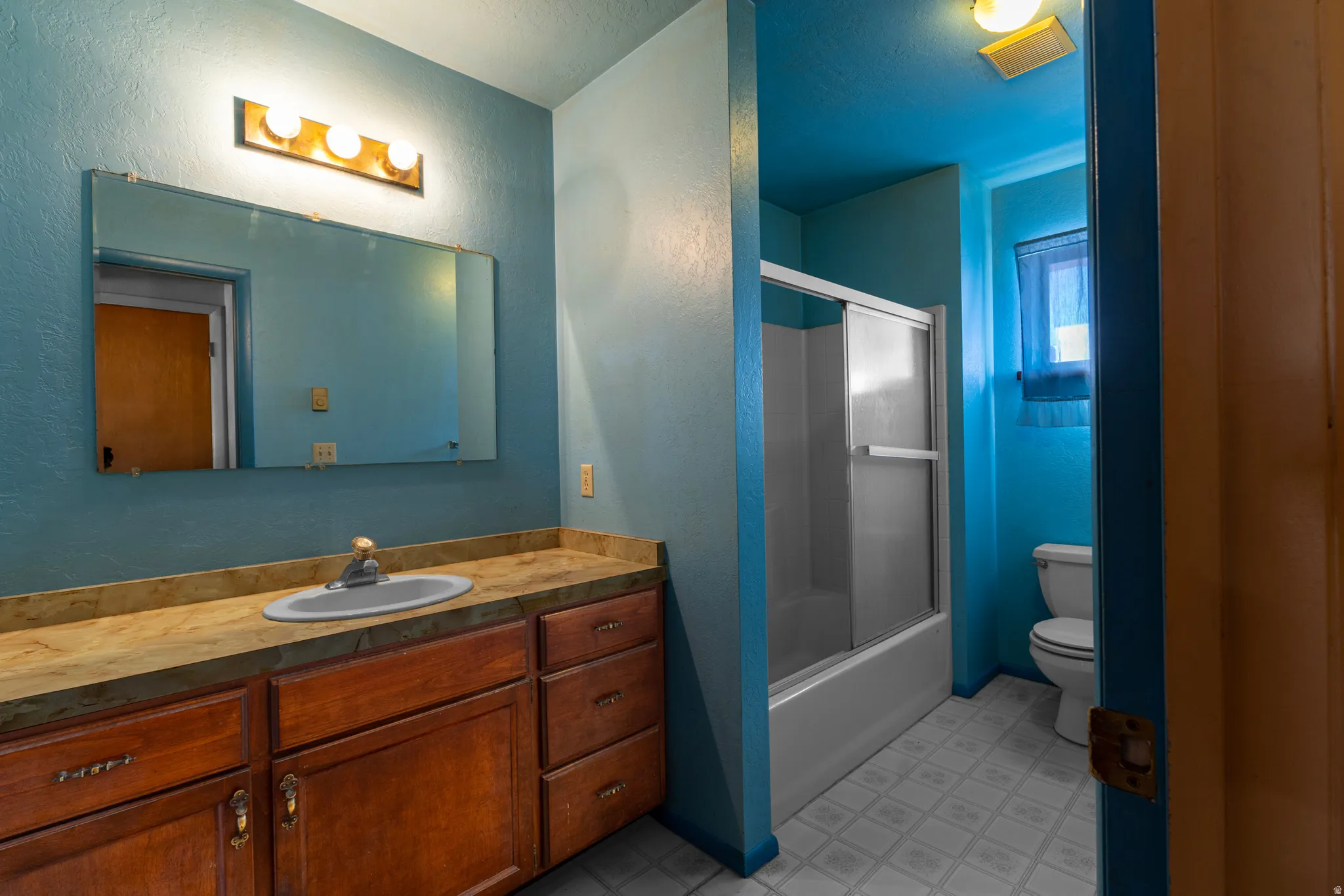 Bathroom with vanity, combined bath / shower with glass door, a textured wall, and light flooring