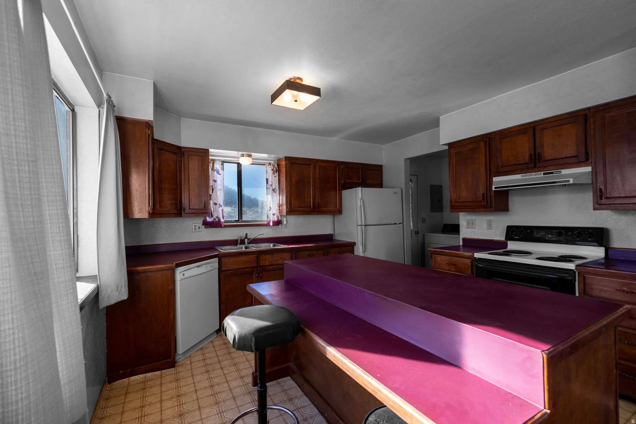Kitchen with light flooring, white appliances, dark countertops, under cabinet range hood, and washer / clothes dryer