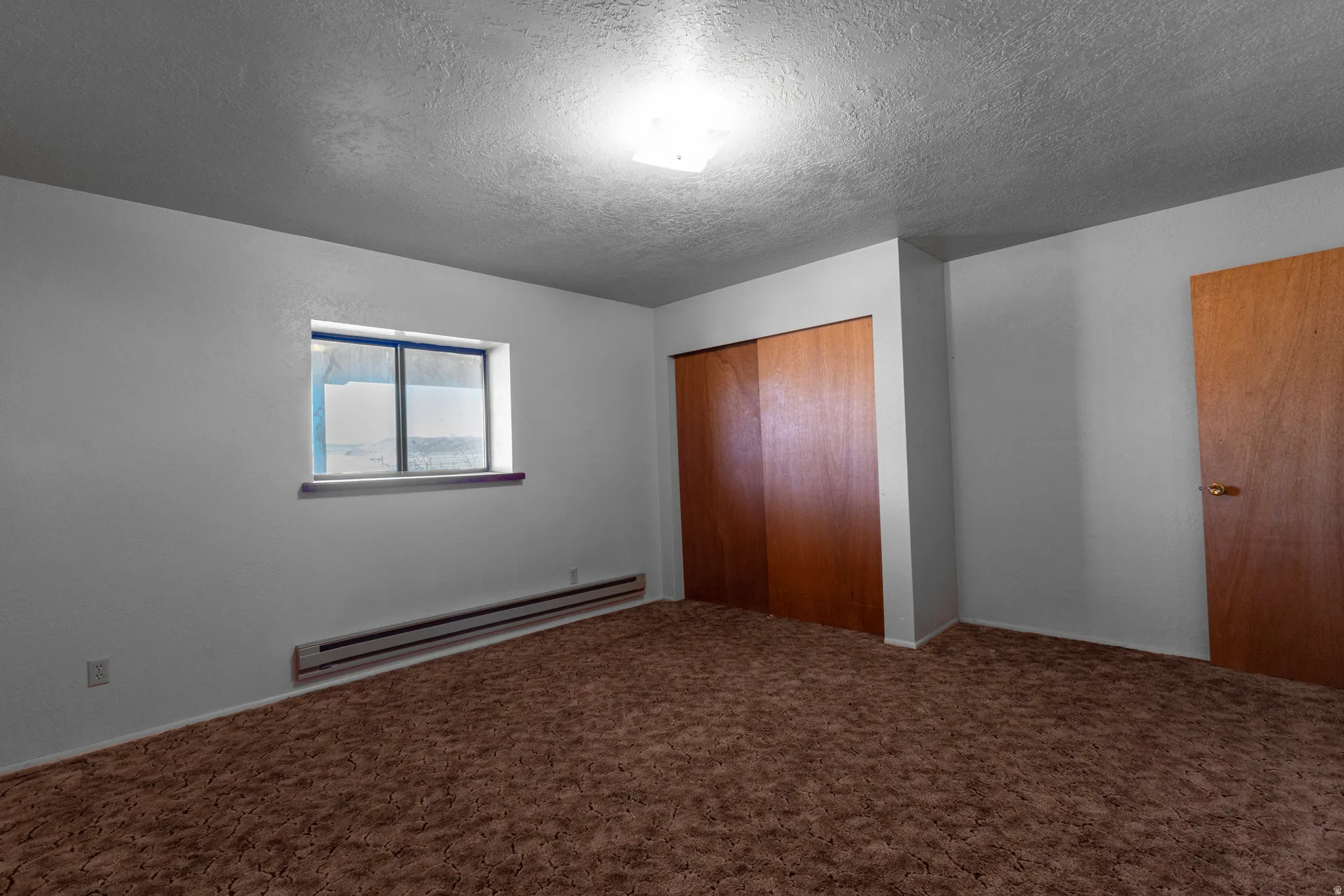 Unfurnished bedroom featuring a baseboard radiator, a textured ceiling, a closet, and carpet flooring