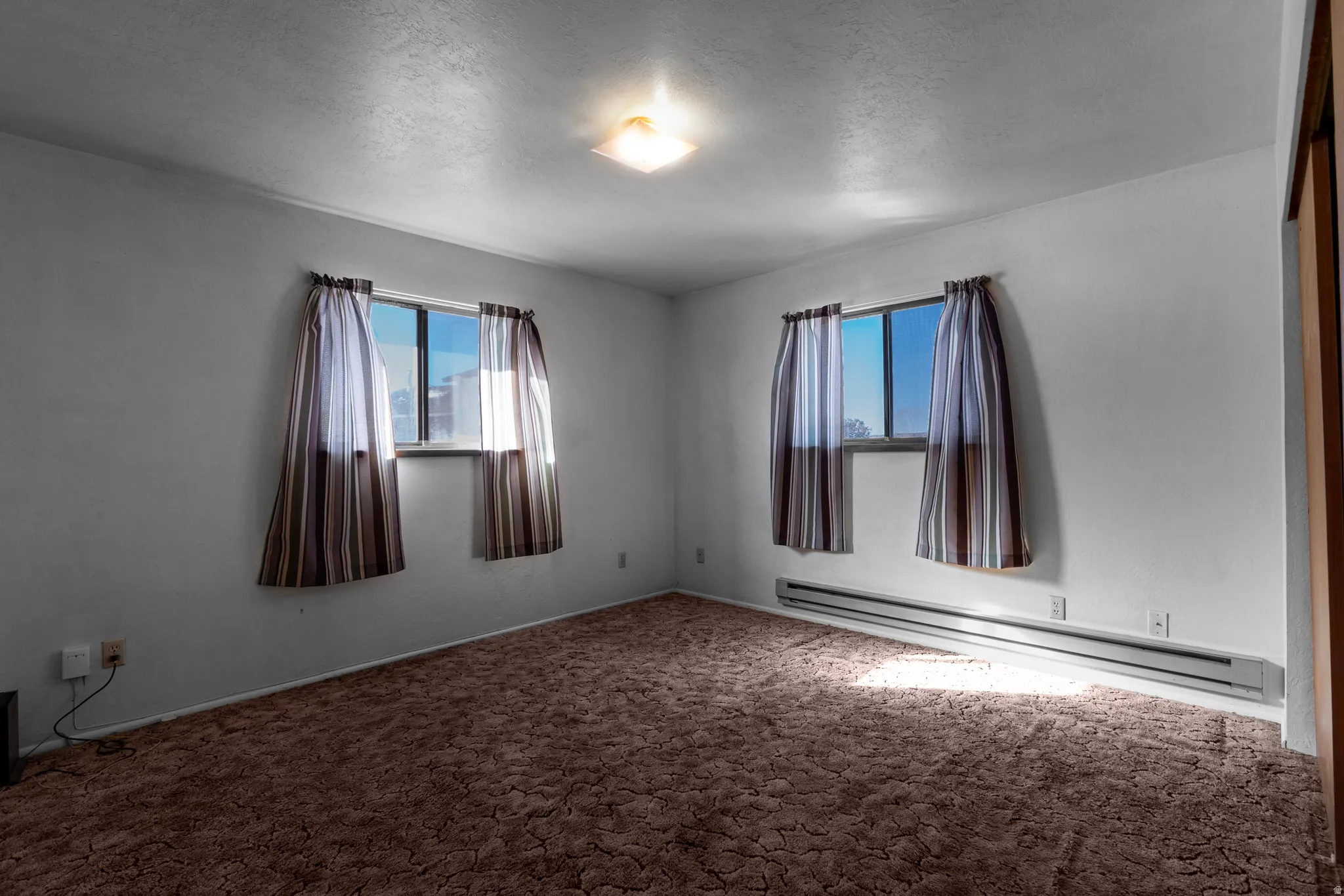 Carpeted spare room featuring a baseboard radiator and a textured ceiling