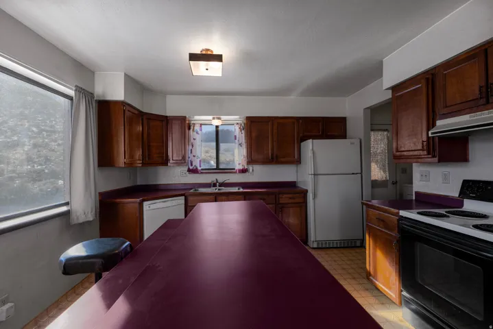 Kitchen with light flooring, white appliances, dark countertops, and under cabinet range hood