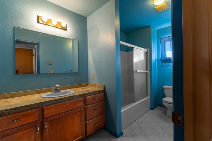 Bathroom with vanity, combined bath / shower with glass door, a textured wall, and light flooring