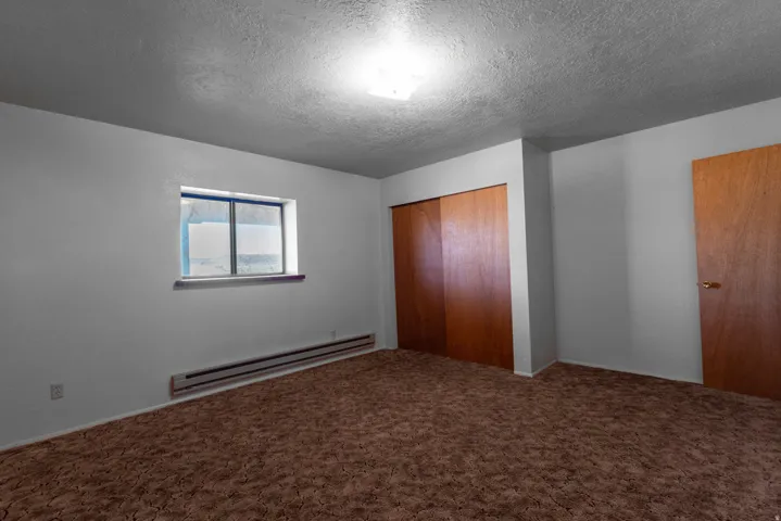 Unfurnished bedroom featuring a baseboard radiator, a textured ceiling, a closet, and carpet flooring