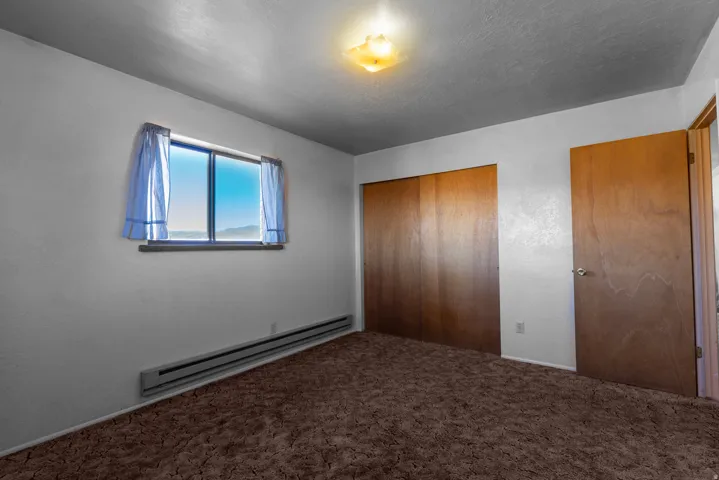 Unfurnished bedroom featuring a baseboard radiator, a closet, a textured ceiling, and carpet