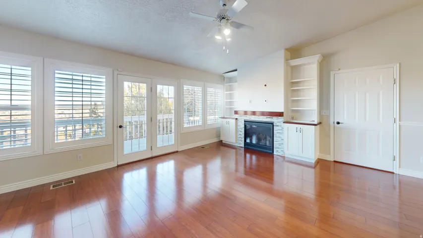 Unfurnished living room with built in features, a textured ceiling, hardwood / wood-style floors, a glass covered fireplace, and a ceiling fan