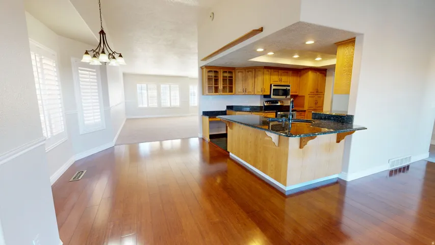 Kitchen featuring brown cabinetry, a kitchen bar, dark stone countertops, decorative light fixtures, and recessed lighting