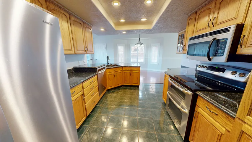 Kitchen with stainless steel appliances, a peninsula, a textured ceiling, recessed lighting, and dark tile patterned flooring