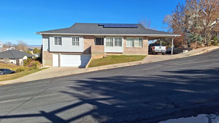 View of front facade with brick siding, solar panels, concrete driveway, and a carport