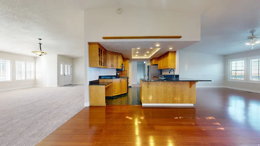 Kitchen featuring open floor plan, brown cabinetry, a breakfast bar area, a textured ceiling, and dark wood-style flooring