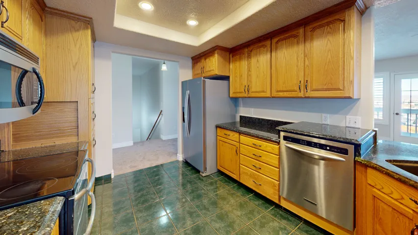 Kitchen with stainless steel appliances, a textured ceiling, dark stone counters, brown cabinetry, and recessed lighting