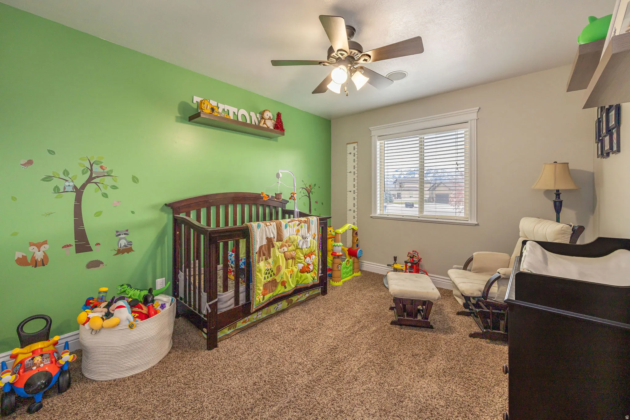Bedroom featuring a nursery area, a ceiling fan, and carpet flooring