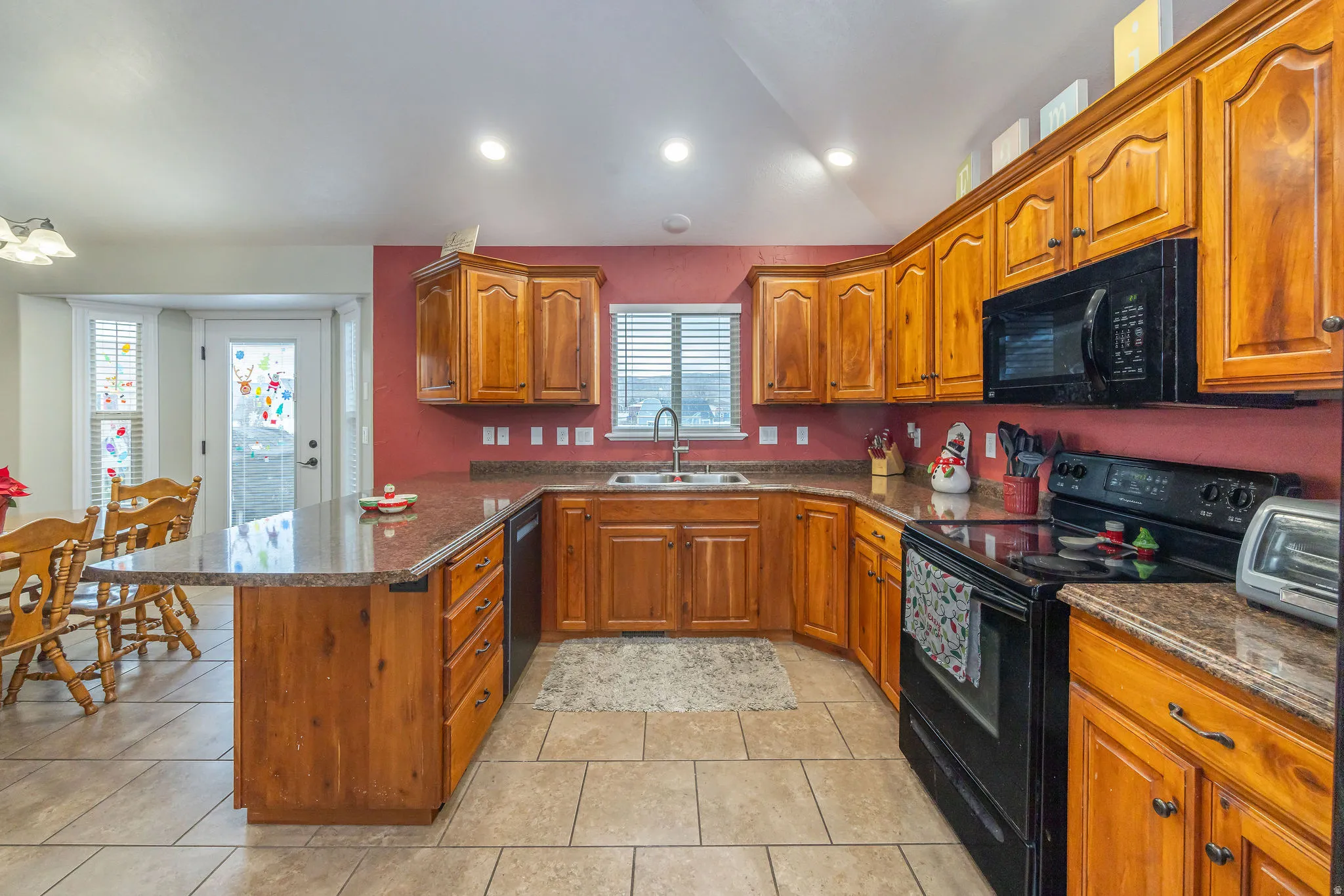 Kitchen featuring dark stone counters, black appliances, brown cabinets, a peninsula, and vaulted ceiling