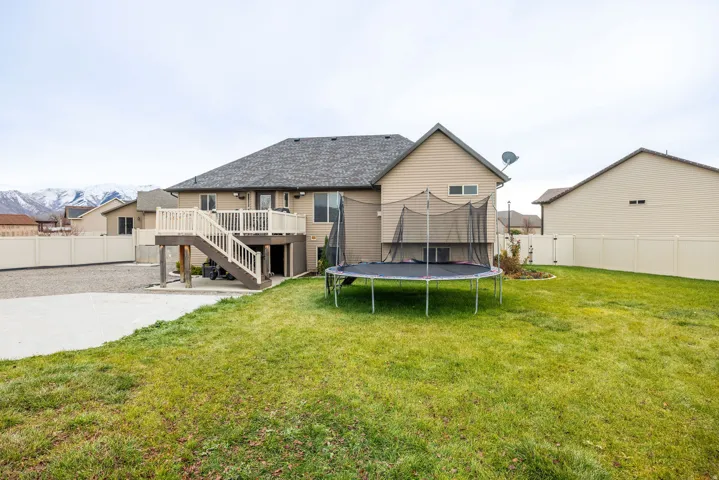 Rear view of house with a fenced backyard, a trampoline, a patio, a deck, and stairs