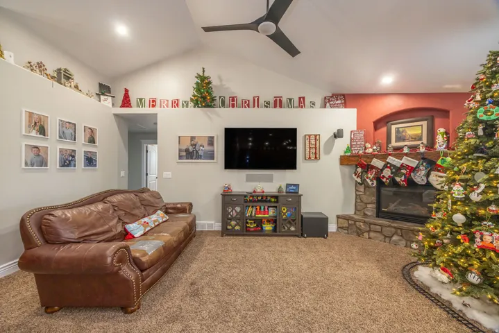 Carpeted living area with vaulted ceiling, a stone fireplace, and ceiling fan