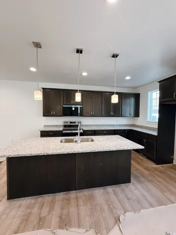Kitchen featuring decorative light fixtures, a kitchen island with sink, light wood-style flooring, and stainless steel appliances