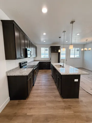 Kitchen featuring black electric range oven, light stone counters, decorative light fixtures, a kitchen island with sink, and light wood-style floors