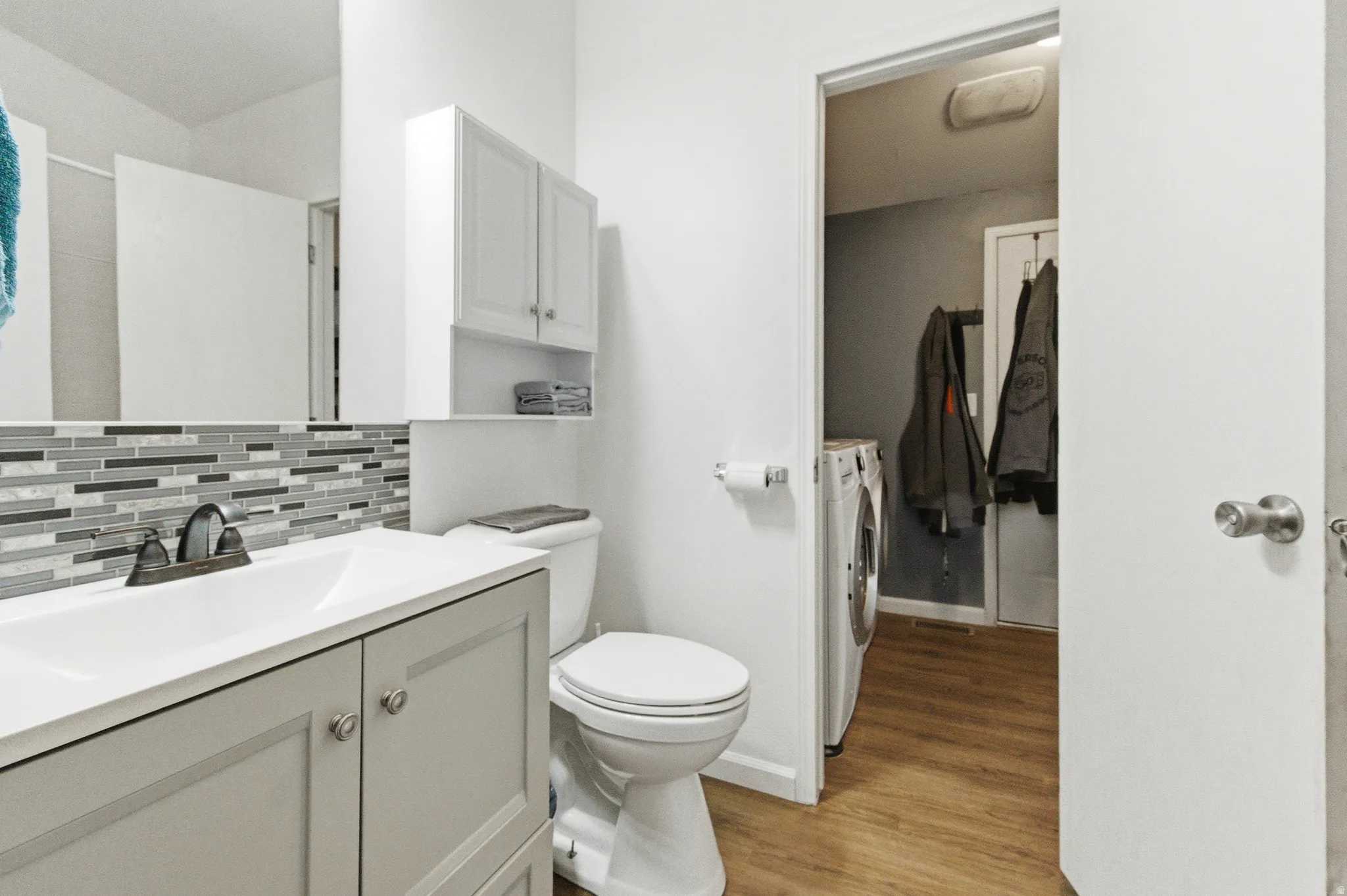 Full bath featuring vanity, decorative backsplash, light wood finished floors, and independent washer and dryer