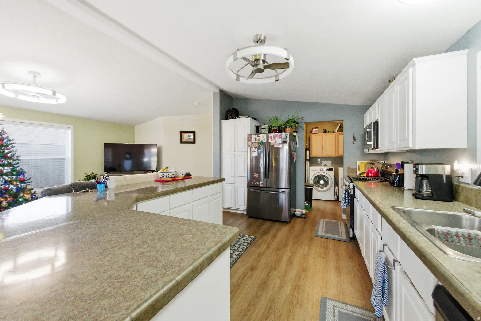 Kitchen featuring white cabinets, stainless steel appliances, vaulted ceiling, washer / dryer, and light wood-style flooring
