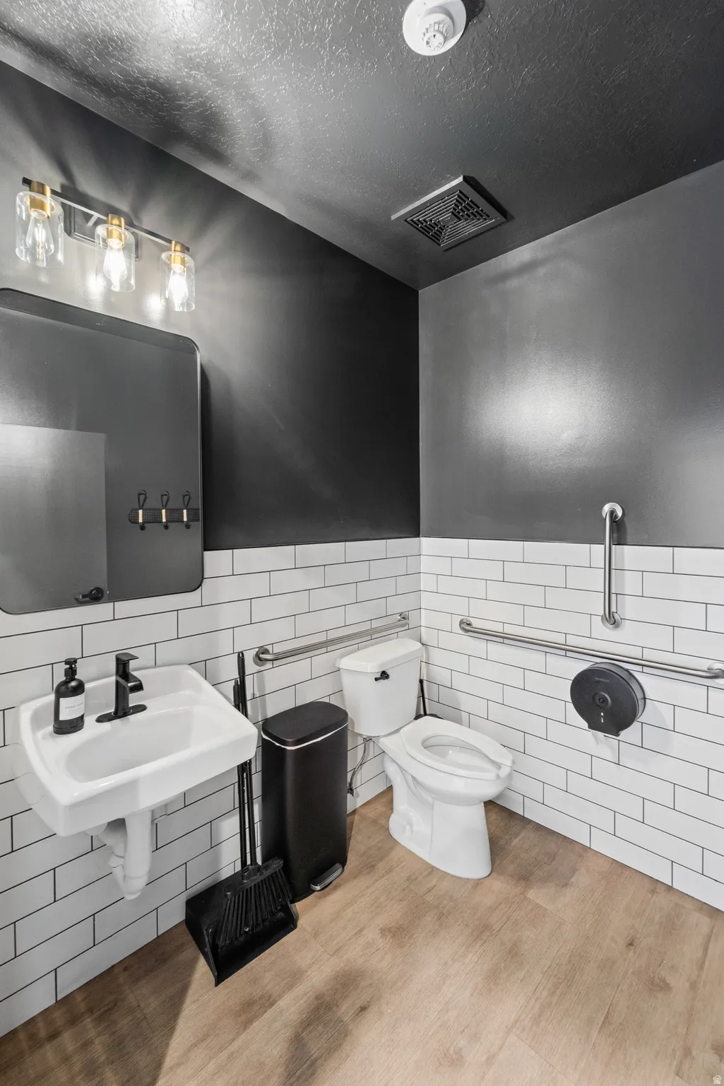 Half bath featuring tile walls, wainscoting, a textured ceiling, and wood finished floors