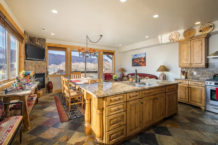 Kitchen with light stone counters, a fireplace, recessed lighting, tasteful backsplash, and a kitchen island with sink