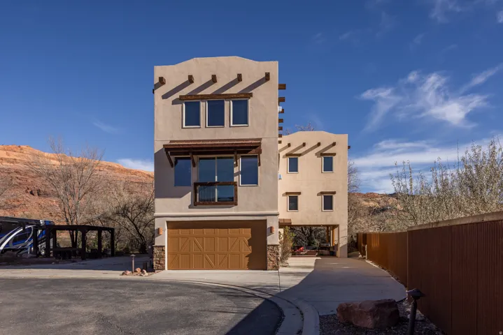 Pueblo revival-style home with concrete driveway, stucco siding, an attached garage, a mountain view, and stone siding