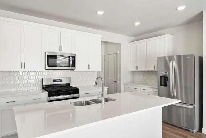 **DISLCAIMER** Exterior & Interior packages may vary.Kitchen with backsplash, appliances with stainless steel finishes, white cabinets, a kitchen island with sink, and recessed lighting