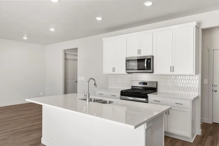 **DISLCAIMER** Exterior & Interior packages may vary.Kitchen with appliances with stainless steel finishes, a center island with sink, white cabinets, dark wood-type flooring, and tasteful backsplash