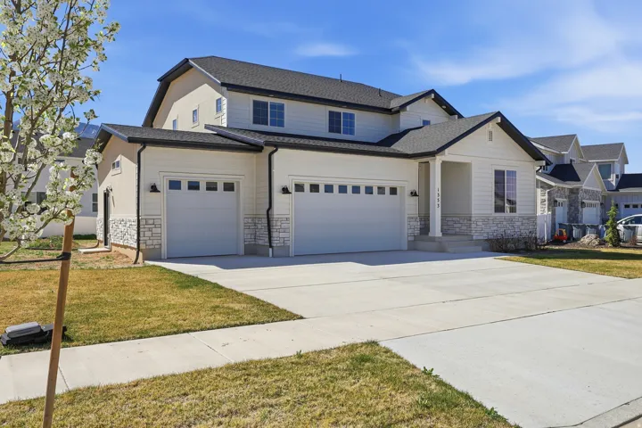 View of front of home featuring stone siding, driveway, a front yard, and roof with shingles
