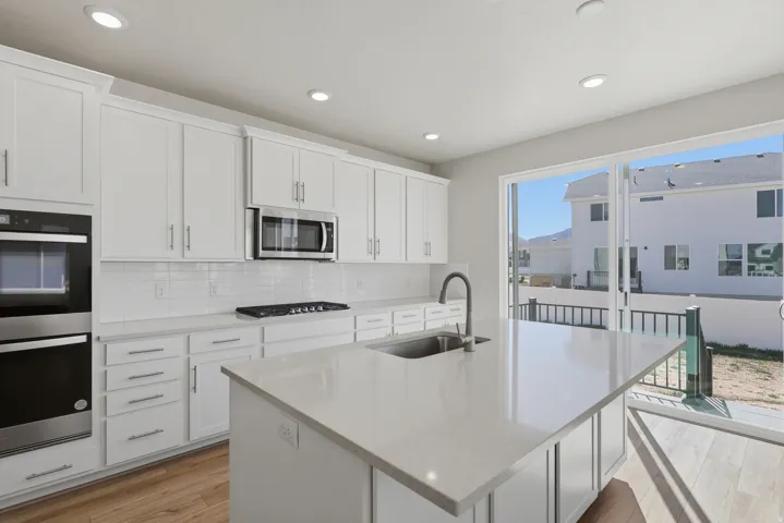 Kitchen featuring light stone counters, stainless steel appliances, white cabinetry, decorative backsplash, and an island with sink