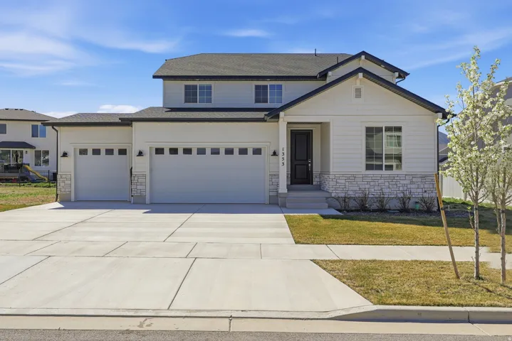 Traditional-style house with a front yard, stone siding, concrete driveway, and a garage