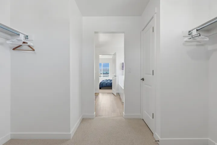 View 2 Primary Suite WIC with Linnen closet featuring light colored carpet and baseboards