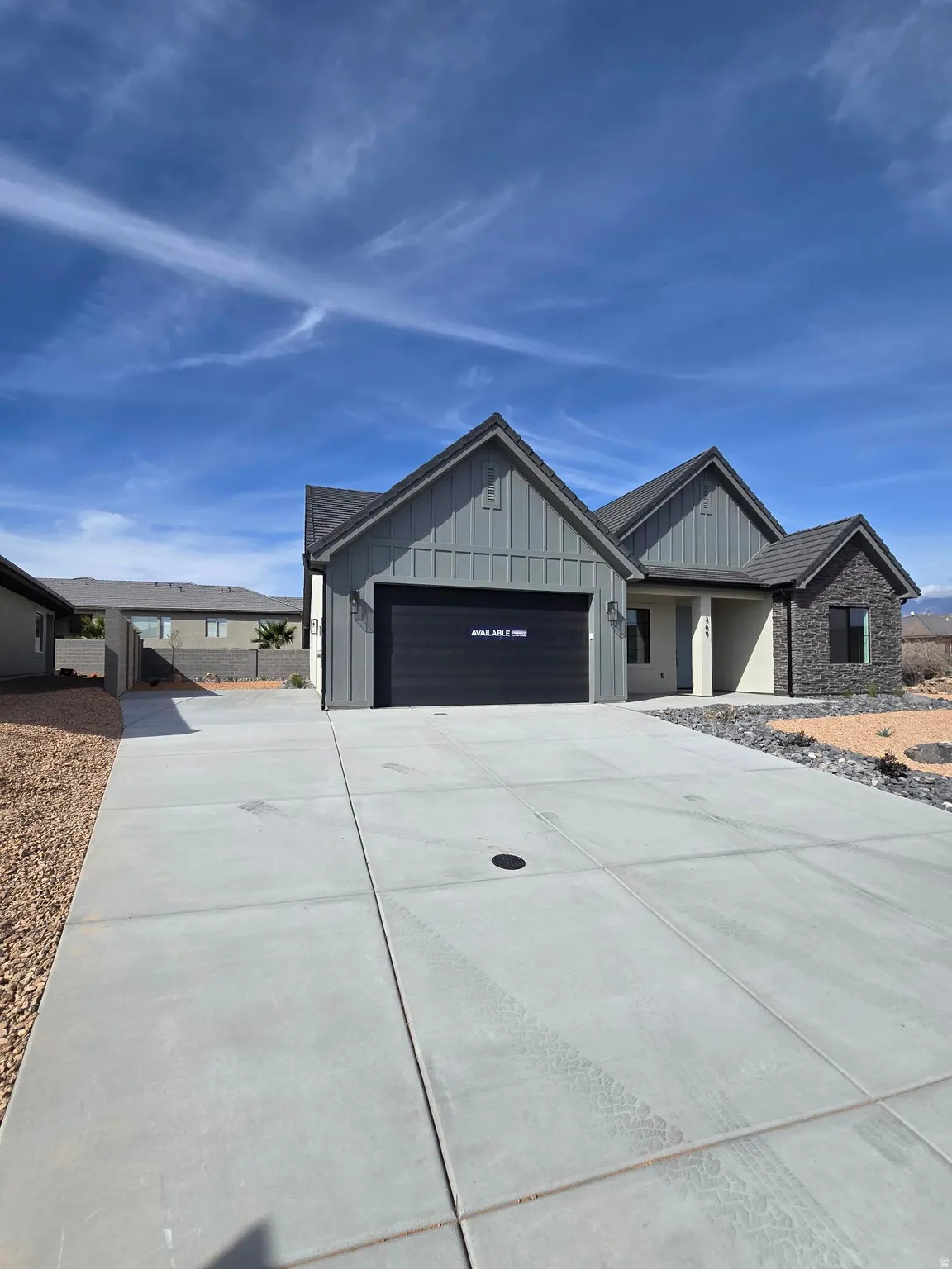 View of front facade with board and batten siding, concrete driveway, an attached garage, and stone siding