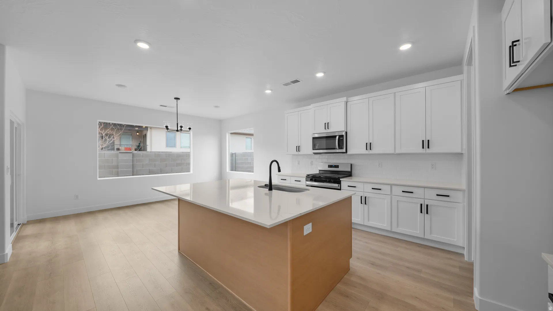 Dual tone kitchen featuring stainless steel appliances, an island with sink, light wood-style flooring, light stone countertops, and two tone cabinetry