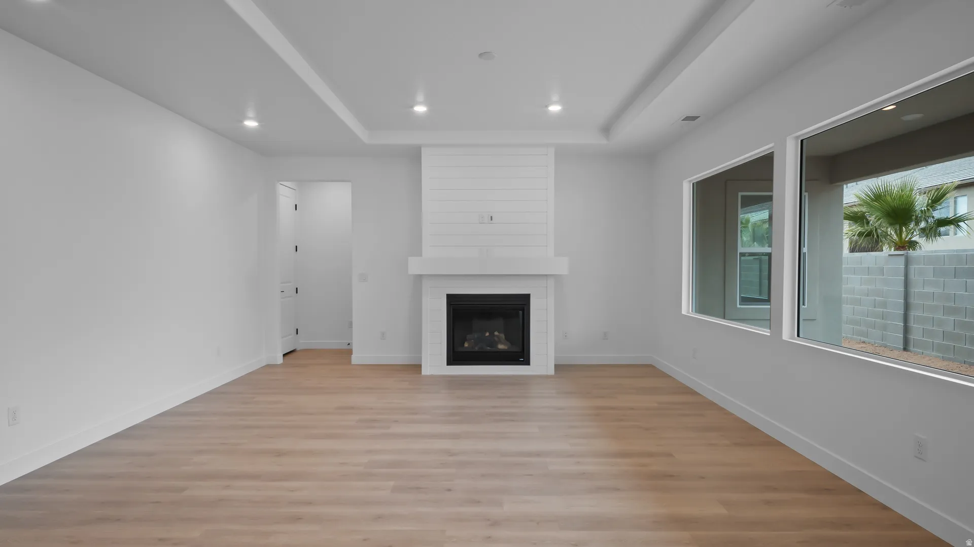 Unfurnished living room with light wood-style flooring, a fireplace, recessed lighting, and a raised ceiling
